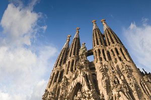 The spires of sagrada família against a blue sky with clouds.